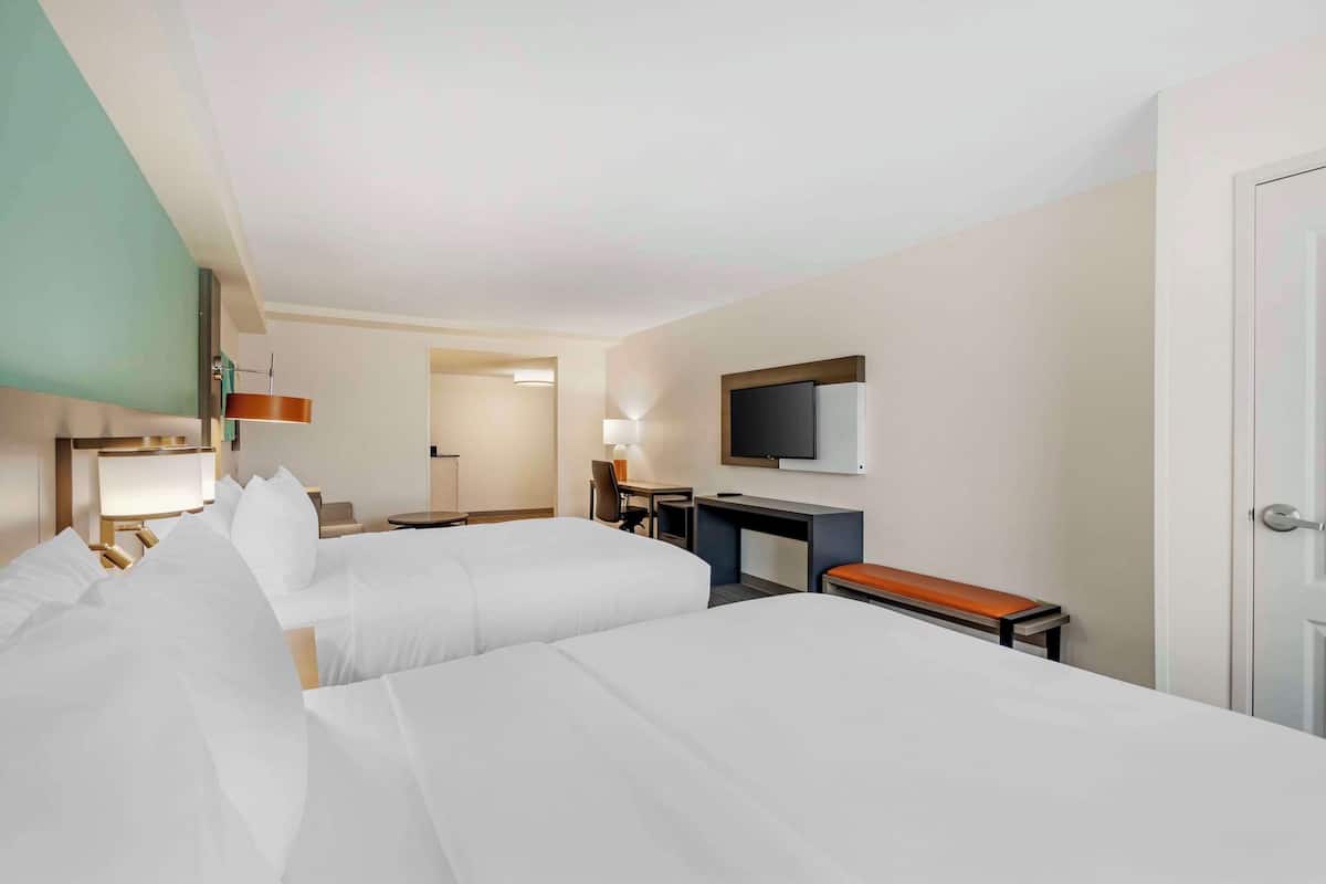 A hotel room with two beds, a desk, a television, and a door.