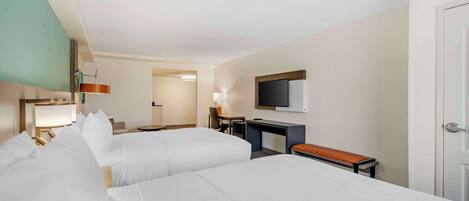 Habitación de hotel con dos camas, un escritorio, televisor y una puerta.