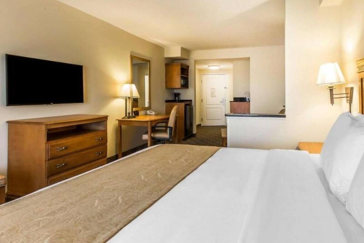 A hotel room with a bed, a desk, a television, a lamp, and a kitchenette.