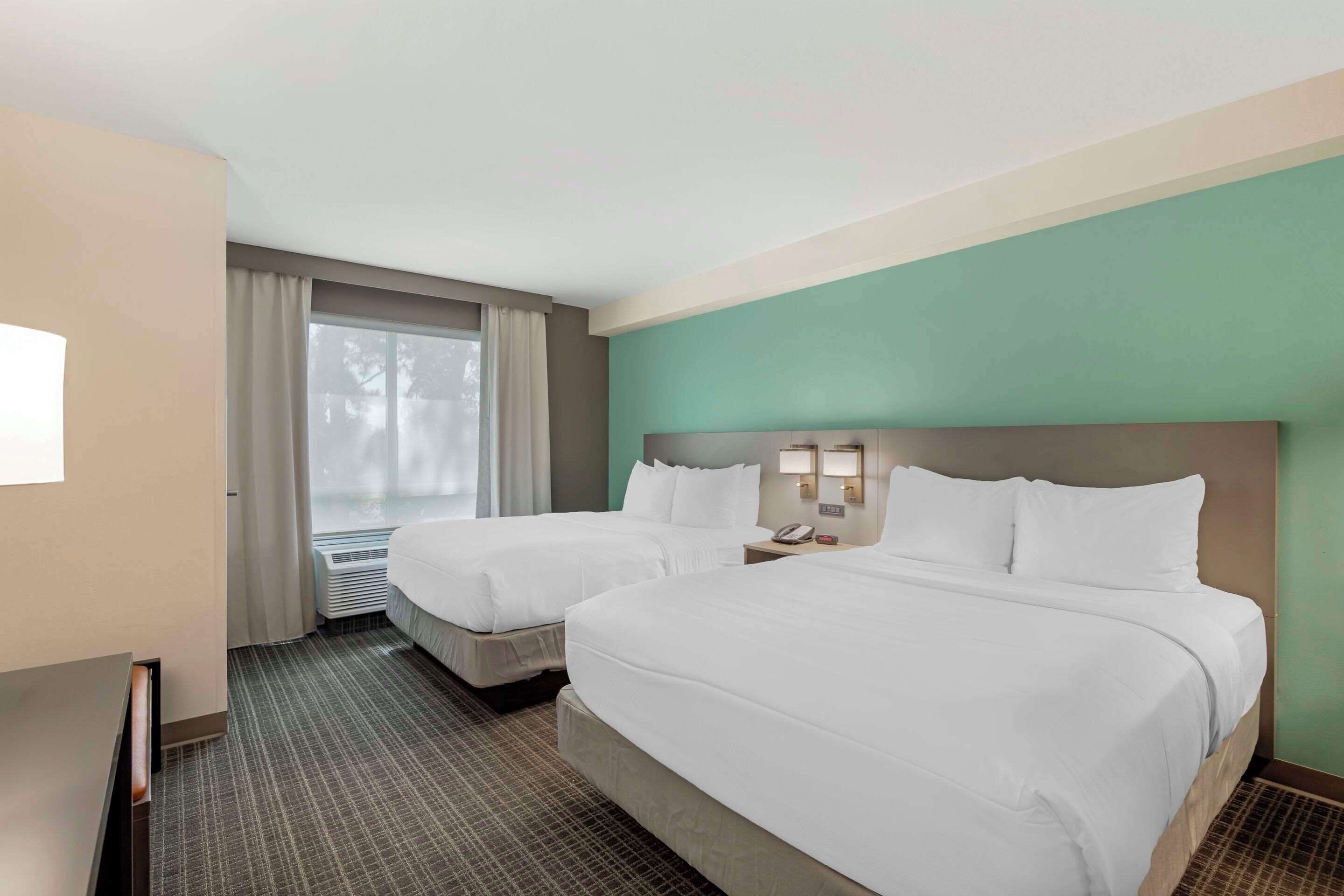 Habitación de hotel con dos camas, un ventanal con cortinas, un escritorio y un teléfono en la pared.