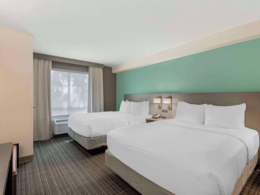 Habitación de hotel con dos camas, un ventanal con cortinas, un escritorio y un teléfono en la pared.