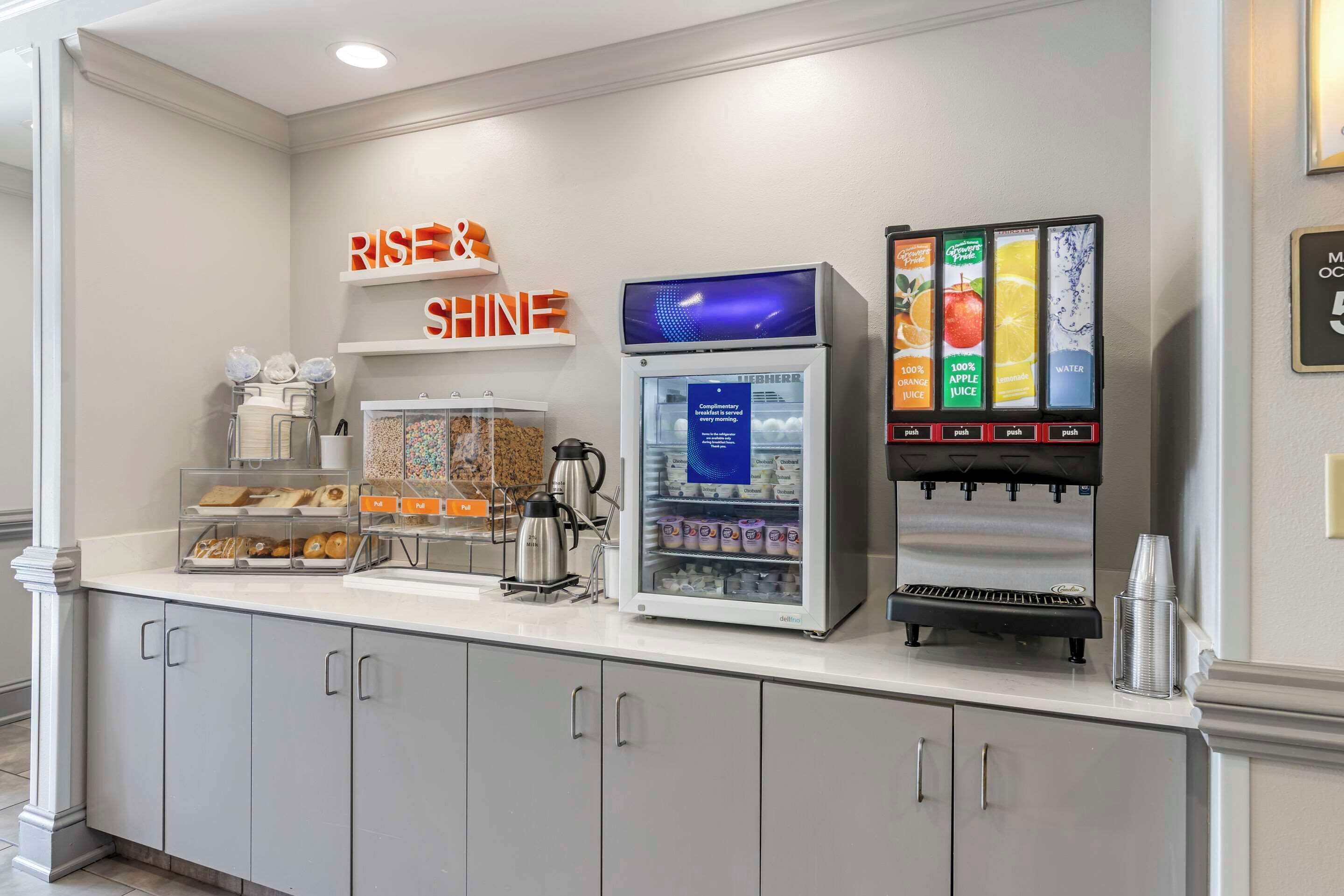 Un comptoir pour le petit-déjeuner équipé d’une machine à café, d’un réfrigérateur-vitrine et d’un distributeur de jus.