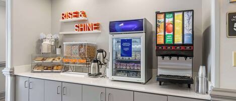 Un comptoir pour le petit-déjeuner équipé d’une machine à café, d’un réfrigérateur-vitrine et d’un distributeur de jus.