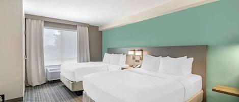 Une chambre d’hôtel avec deux lits, une grande fenêtre avec des rideaux, une table de chevet avec une lampe et une étagère fixée au mur.