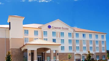 Un hotel con un letrero llamativo que dice "Comfort Suites", que presenta un diseño arquitectónico moderno con numerosas ventanas y una entrada cubierta.