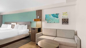 A hotel room with a bed, a sofa, a small table, and artwork on the wall. - Comfort Suites Valdosta Mall Area (Valdosta)