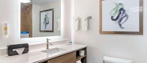 Une salle de bain moderne avec un grand miroir, un lavabo et des toilettes. Un tableau encadré est accroché au mur, et il y a un porte-serviettes.