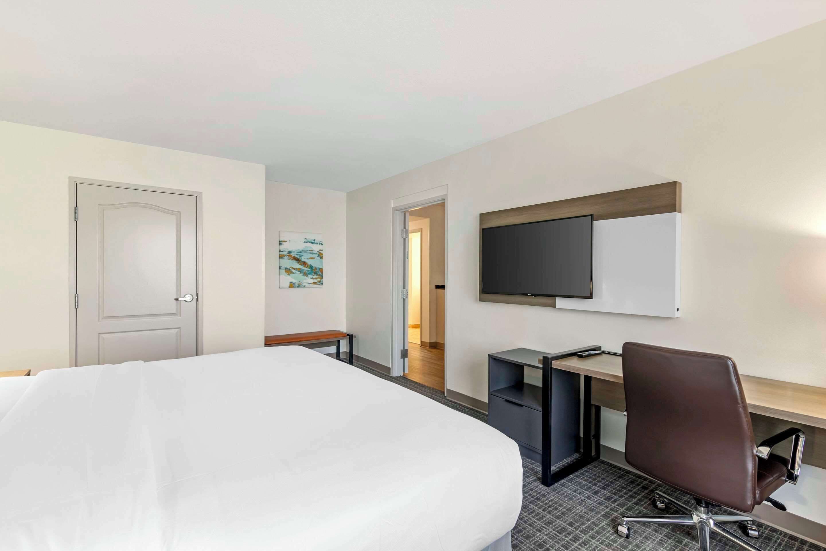 Een hotelkamer met een groot bed, een bureau met stoel, een televisie en een deur.