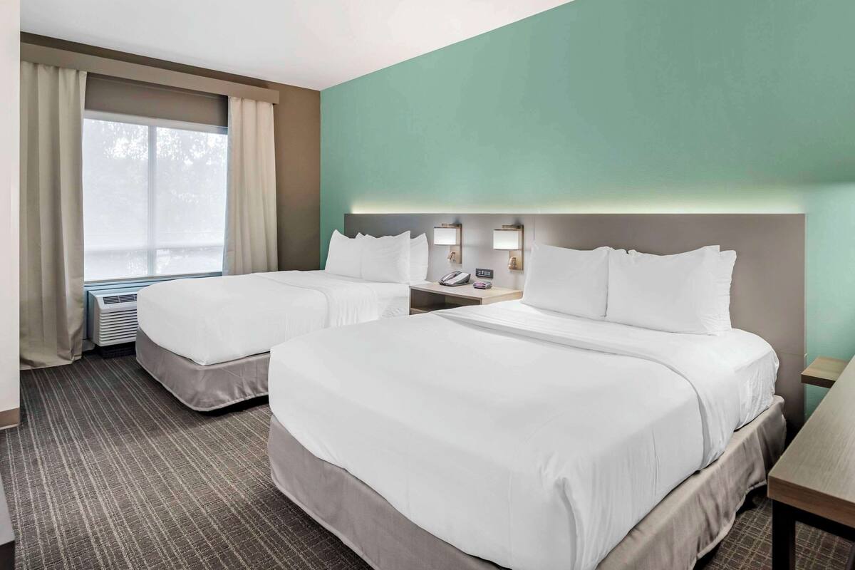 A hotel room with two beds, a large window with curtains, a wall-mounted phone, and a small table.