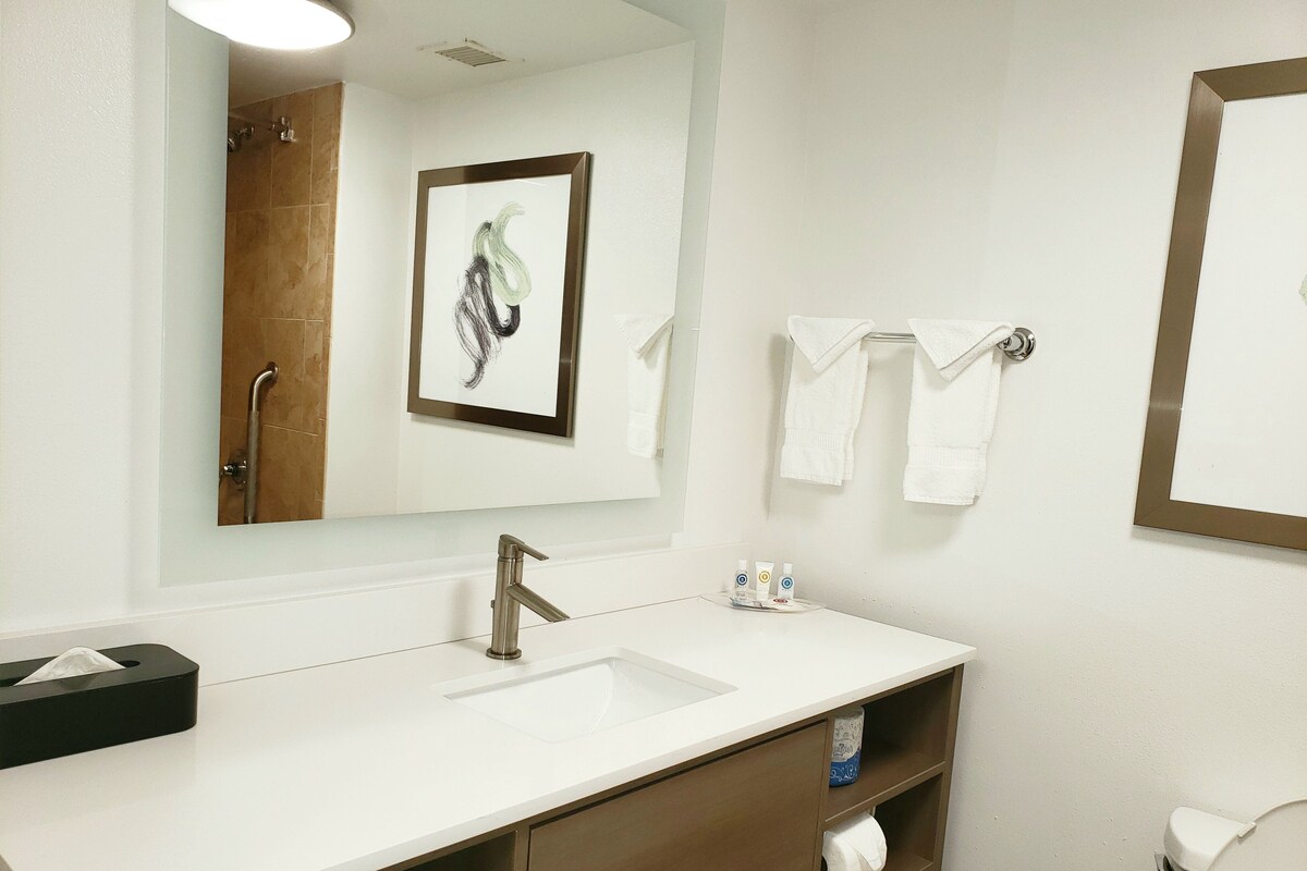 A bathroom with a white sink, a mirror, a framed artwork, and a towel rack.