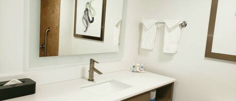 Une salle de bain avec un lavabo blanc, un miroir, une œuvre d’art encadrée et un porte-serviettes.