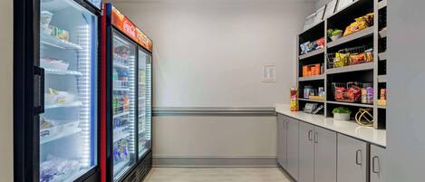 En smal korridor med två automater på ena sidan och hyllor fyllda med snacks på den andra.