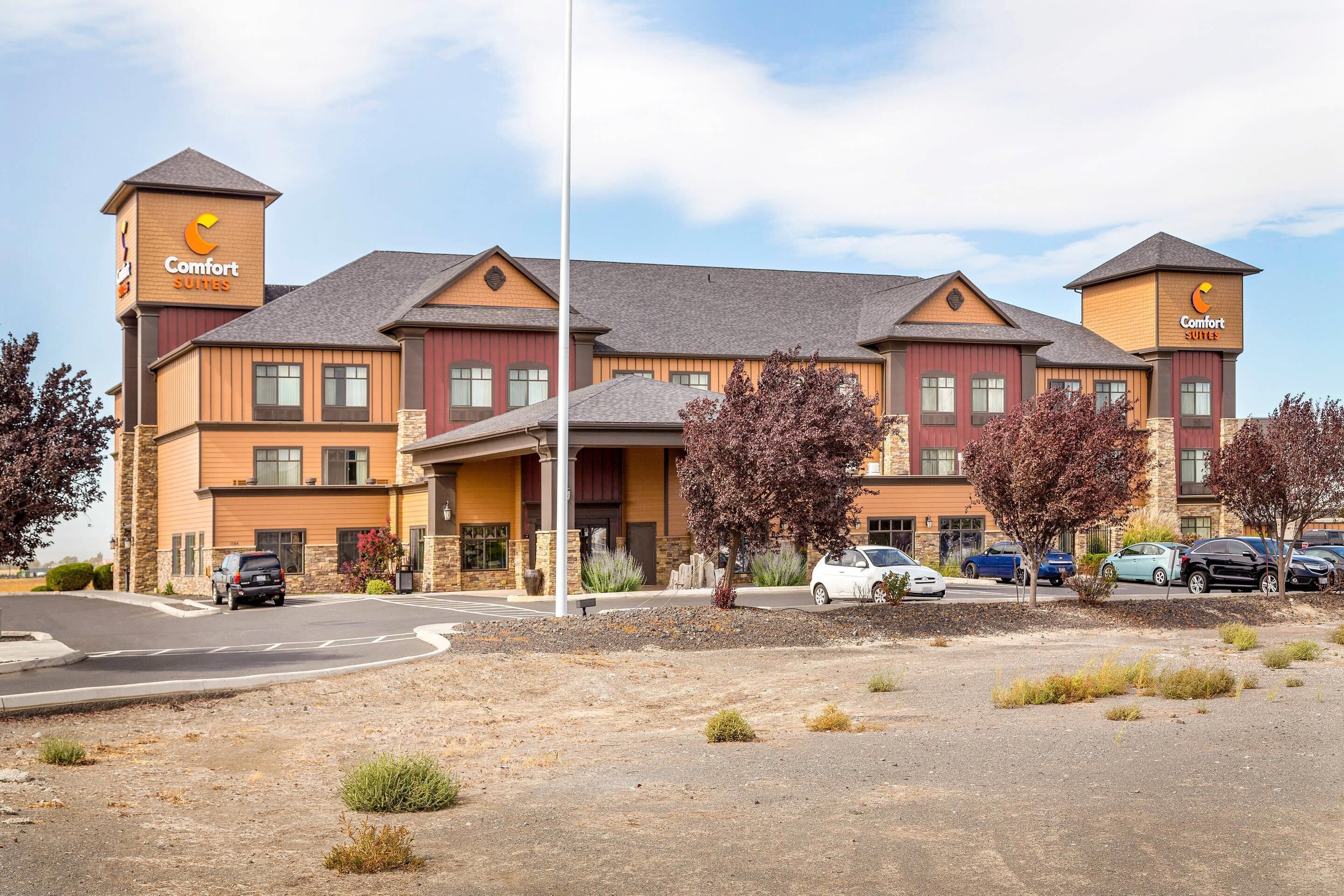 A Comfort Suites hotel with a two-story structure, a parking lot, and a clear sky.
