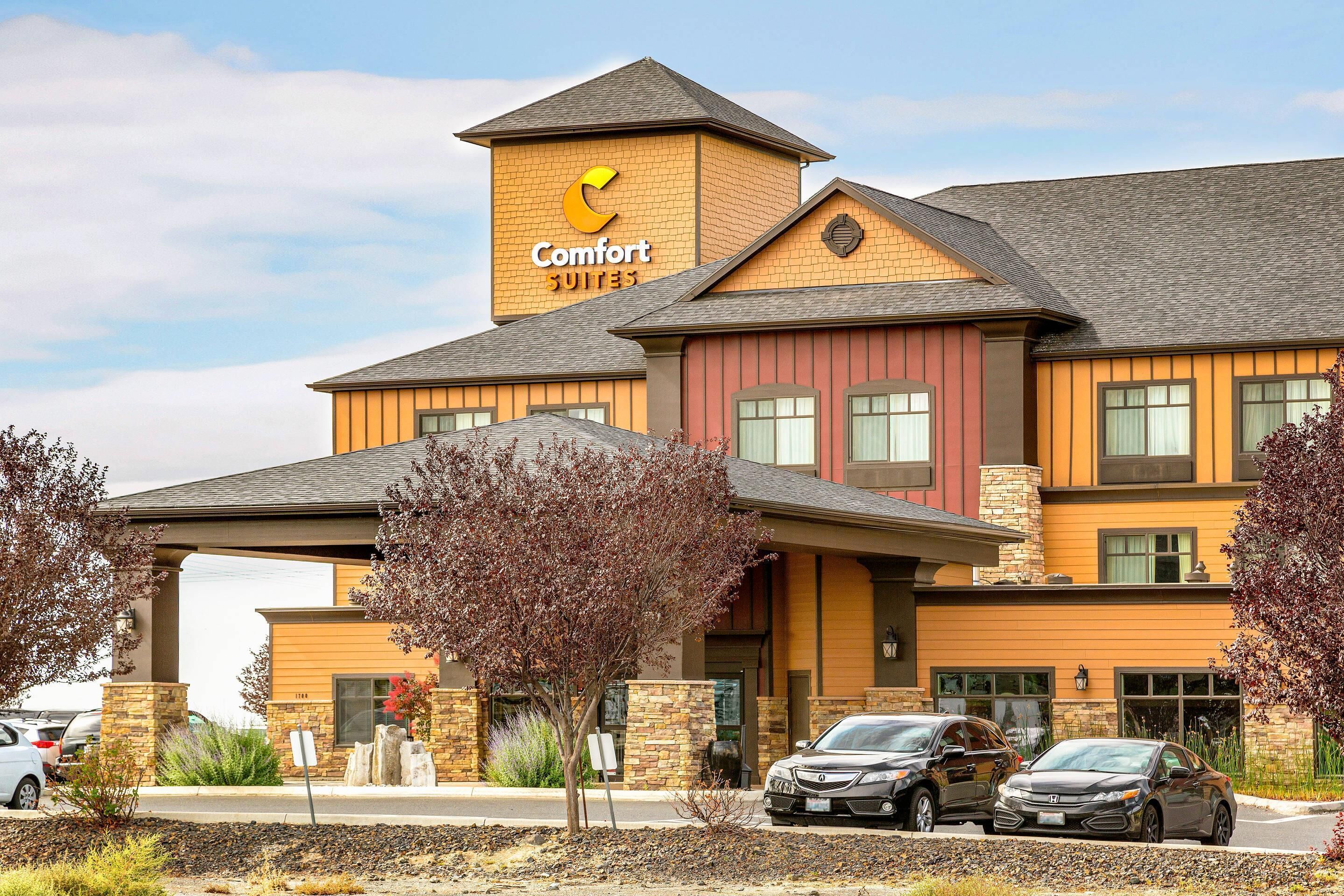 Ein Comfort Suites Hotel mit Backsteinfassade, zahlreichen Fenstern und einem Parkplatz mit Autos.