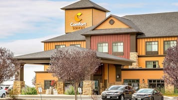 Un hotel Comfort Suites con fachada de ladrillo, múltiples ventanas y un estacionamiento con vehículos.