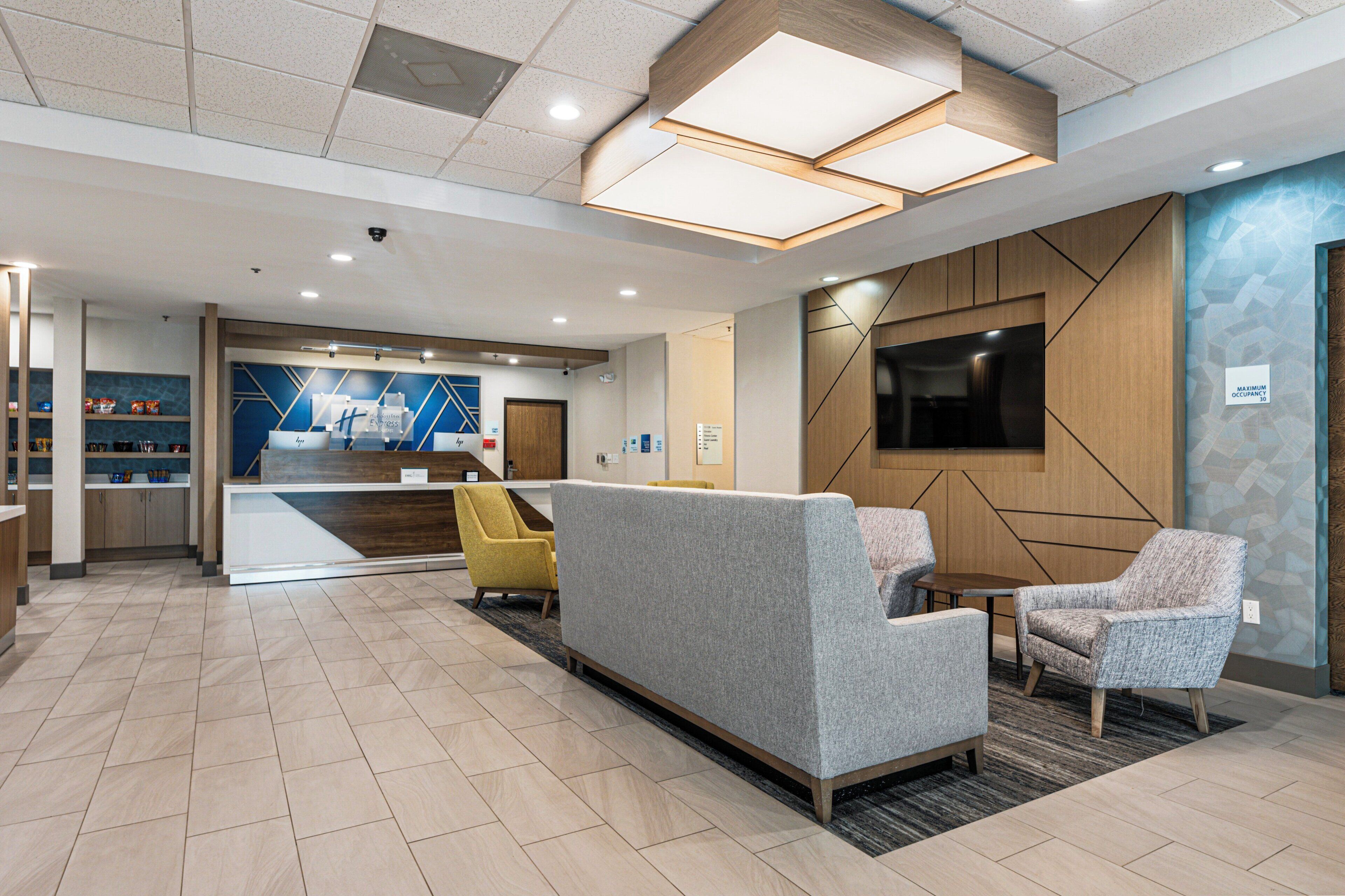 A modern lobby with a reception desk, seating area, and a large TV screen.