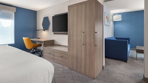 Een hotelkamer met een bed, een bureau met stoel, een kledingkast, een televisie en een blauwe bank.