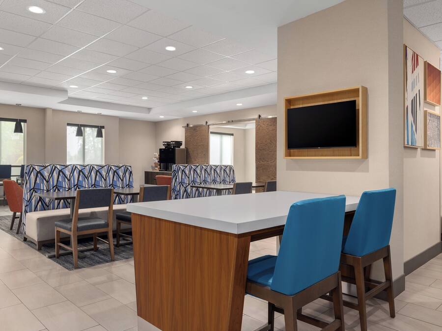 Een moderne hotel eetruimte met een grote rechthoekige tafel, blauwe zitzakstoelen, een aan de muur bevestigde televisie en een kamer met een patroon.