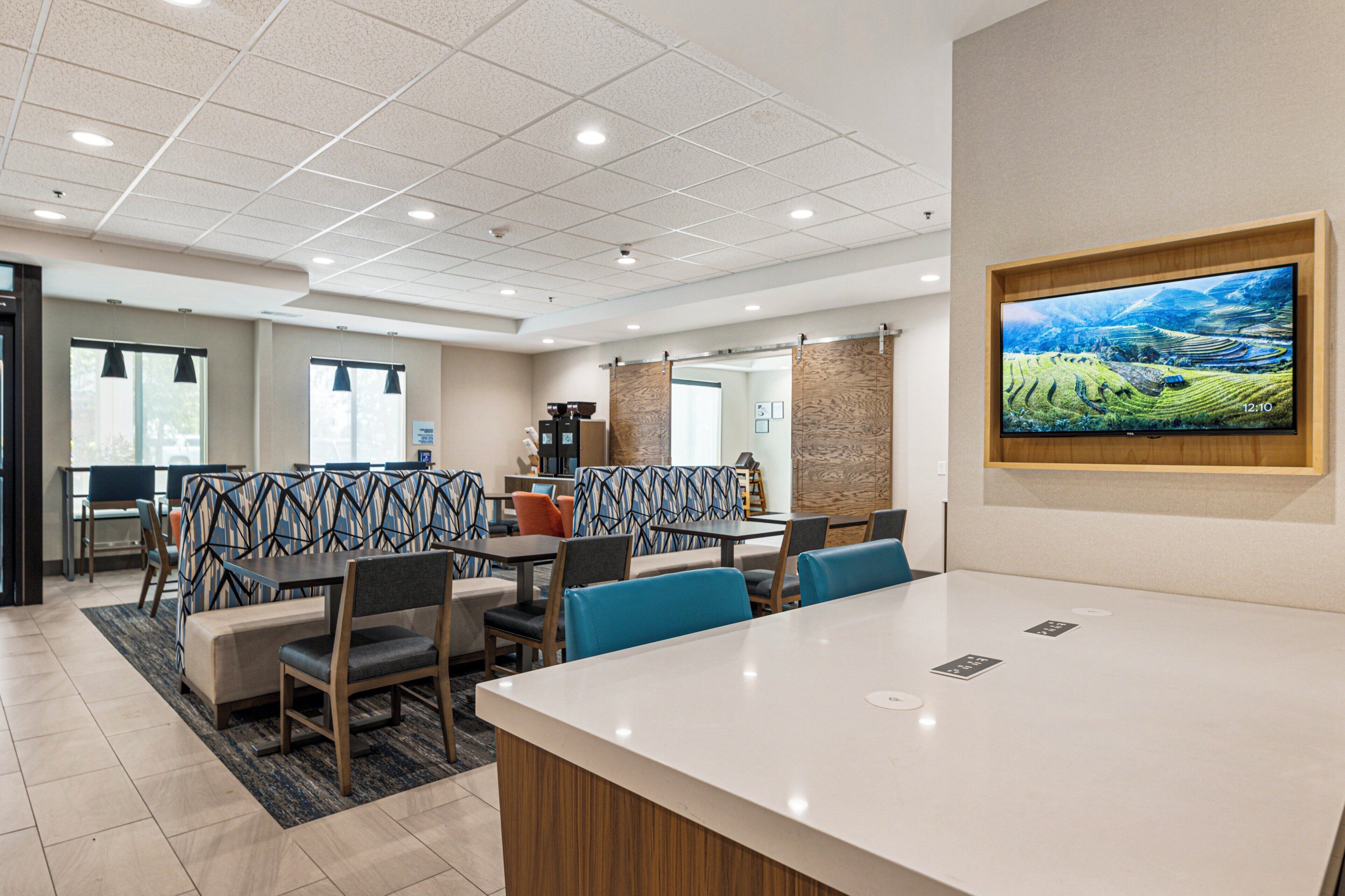Een moderne hotellobby met een ruime receptiebalie, een zithoek met patroonstoelen, en een groot scherm waarop een panoramisch landschap wordt weergegeven.