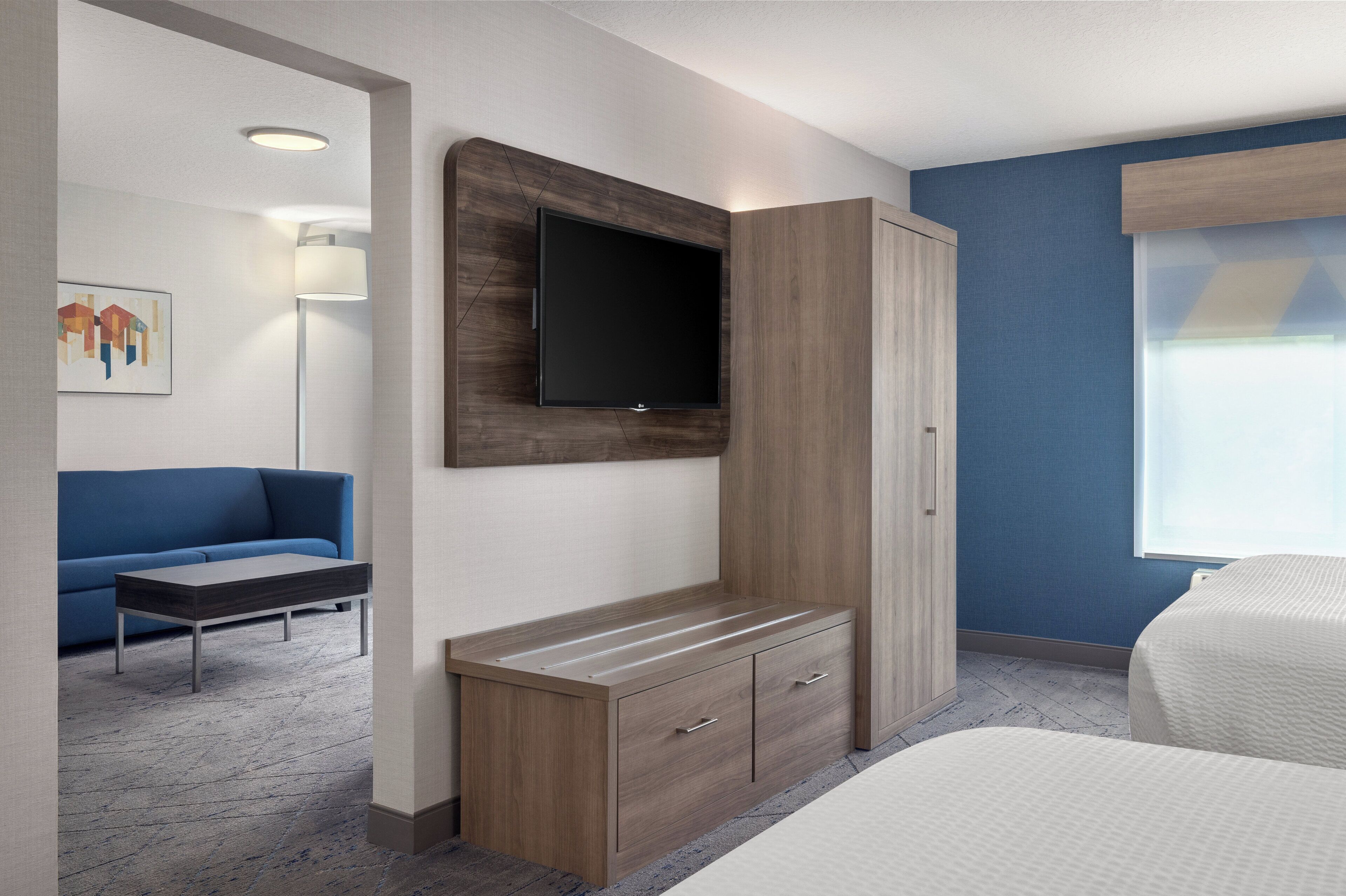 Ein modernes Hotelzimmer mit Flachbildfernseher, Holzschrank, blauem Sofa und Bett.