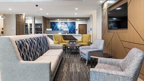 Een moderne hotel lobby met een bank, fauteuils, een salontafel en een aan de muur bevestigde televisie.