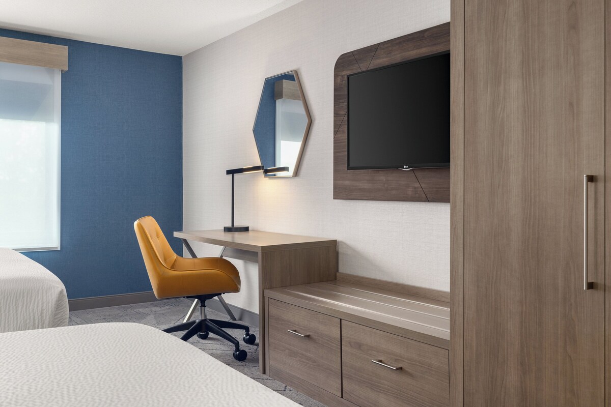 Una habitación de hotel con cama, escritorio, silla, televisor y armario.