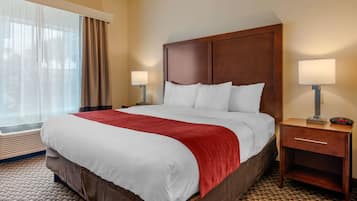 A hotel room with a large bed, two bedside tables with lamps, a red throw blanket, and a window with curtains.