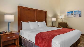 A hotel room with a large bed, wooden headboard, two bedside lamps, a nightstand with a lamp, and two framed pictures on the wall.