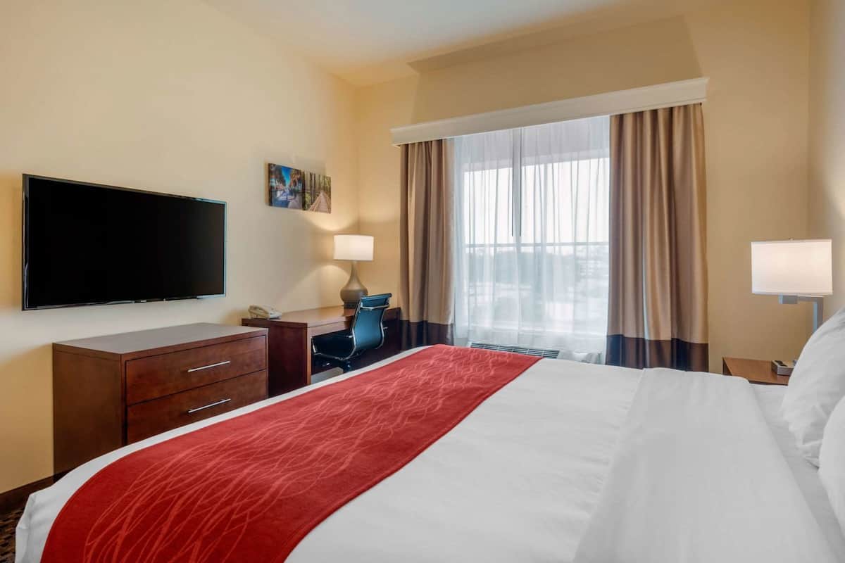 A hotel room with a bed, a desk, a chair, a television, and a window with curtains.