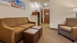 Un hall d’hôtel avec un canapé marron, un fauteuil assorti et une petite table. On y trouve trois tableaux encadrés accrochés au mur, un meuble en bois et un sol recouvert d’une moquette.