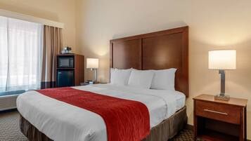 A hotel room with a large bed, two bedside tables, a TV, and a window with curtains.