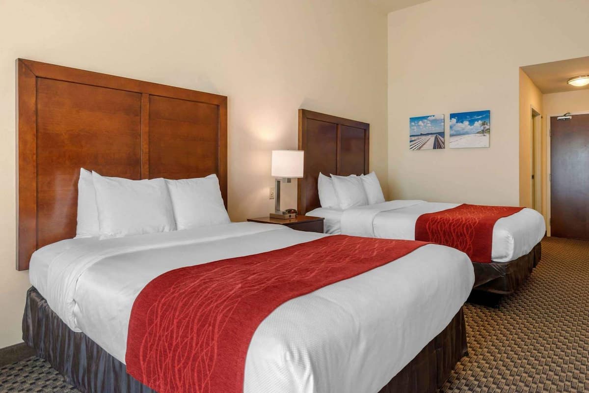A hotel room with two beds, a wooden headboard, a nightstand with a lamp, and two wall-mounted pictures.