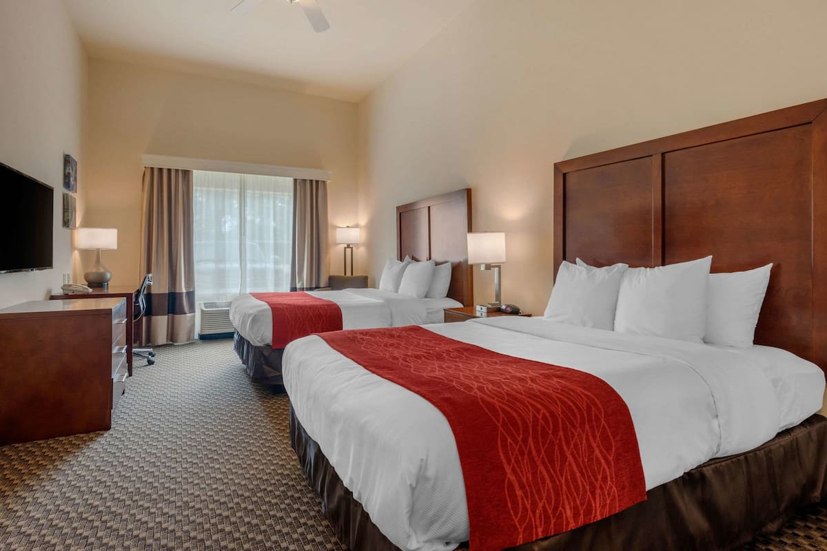 A hotel room with two beds, a desk, a TV, and a window with curtains.