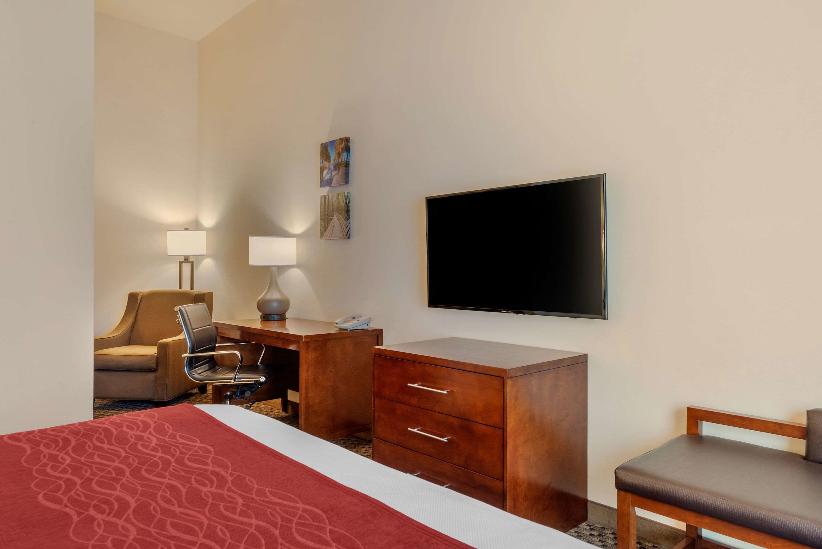 A hotel room with a bed, a desk with a lamp, a chair, a television, and a wooden dresser.