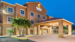 Un hôtel Comfort Inn & Suites doté d’une entrée abritée, de palmiers et d’une façade bien éclairée.