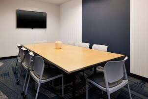 Un salón de conferencias con una mesa larga, seis sillas, un televisor de pantalla plana en la pared y una pared de acento oscura.
