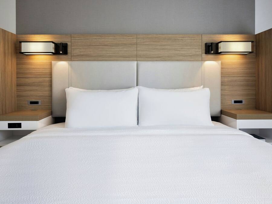 Una habitación de hotel moderna con una cama grande, dos mesitas de noche e iluminación en la pared.