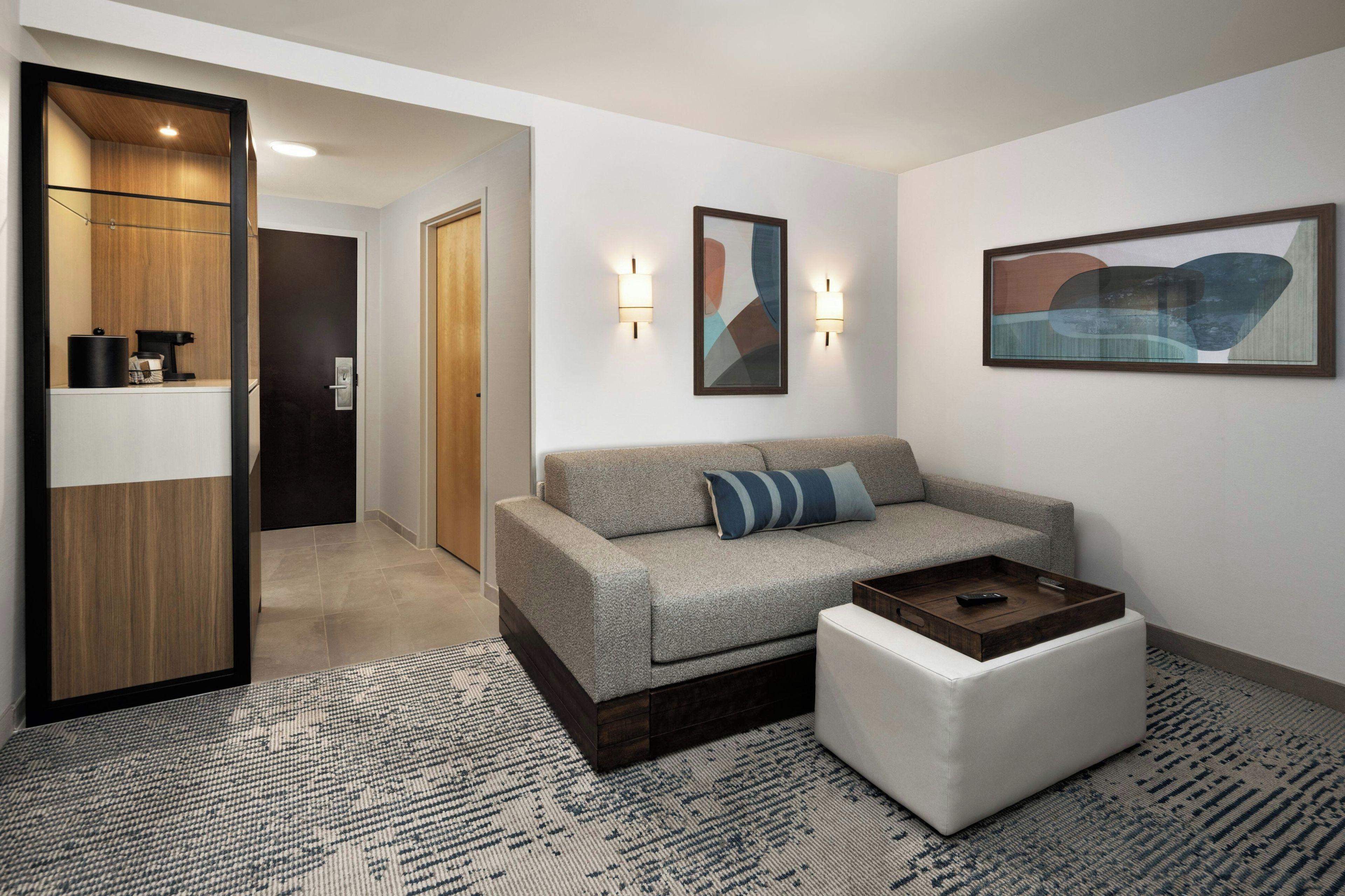 A modern living room with a sofa, ottoman, and coffee table. There is a hallway leading to another room.