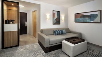 A modern living room with a sofa, ottoman, and coffee table. There is a hallway leading to another room.