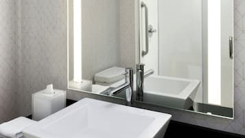 A modern bathroom with a large white sink, a mirror, and a shower.