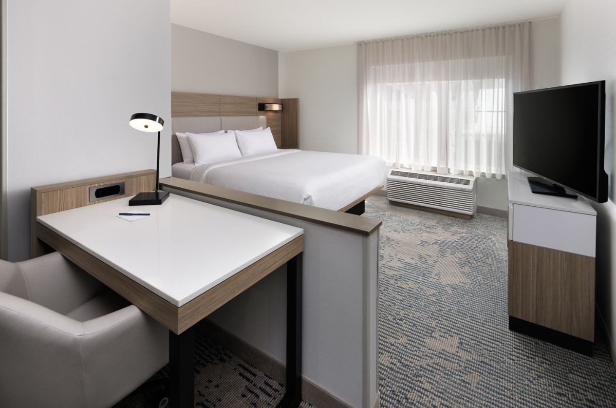 A hotel room with a bed, a desk, a chair, a television, and a window with curtains.