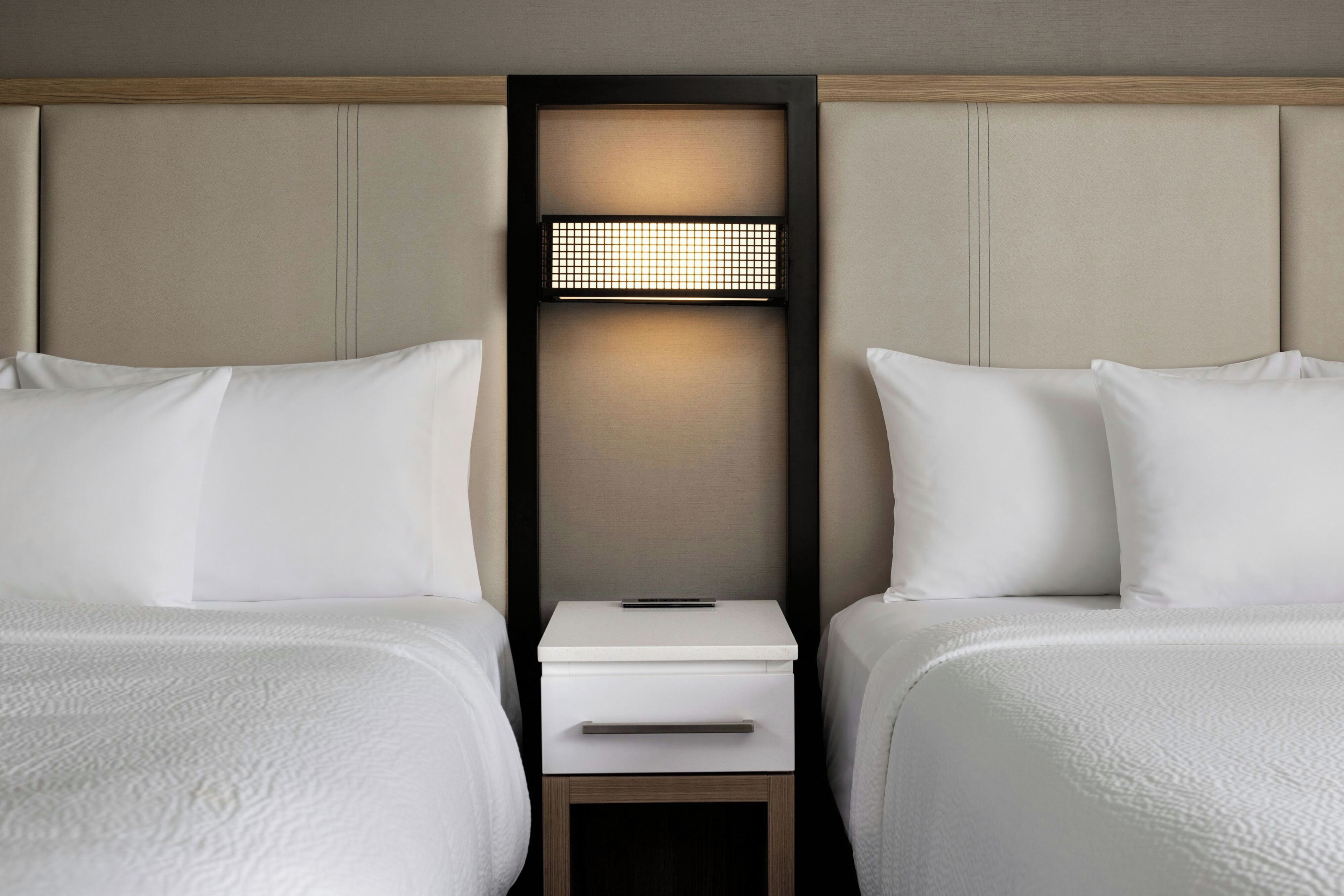 Een hotelkamer met twee bedden, een nachtkastje en een wandlamp.