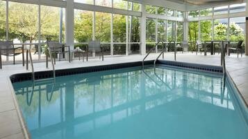 A swimming pool with clear blue water, surrounded by large windows offering views of greenery.