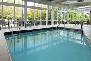 A swimming pool with clear blue water, surrounded by large windows offering views of greenery.