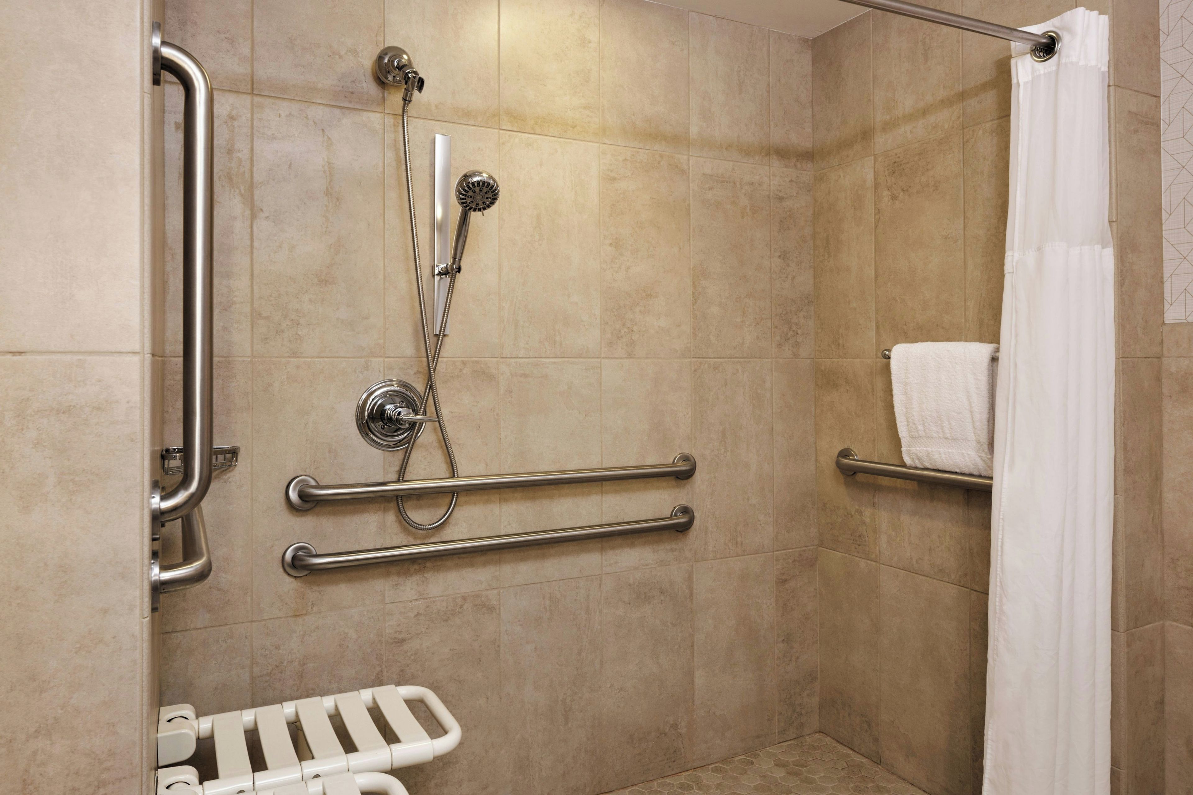A shower area with grab bars, a handheld showerhead, and a white towel rack.