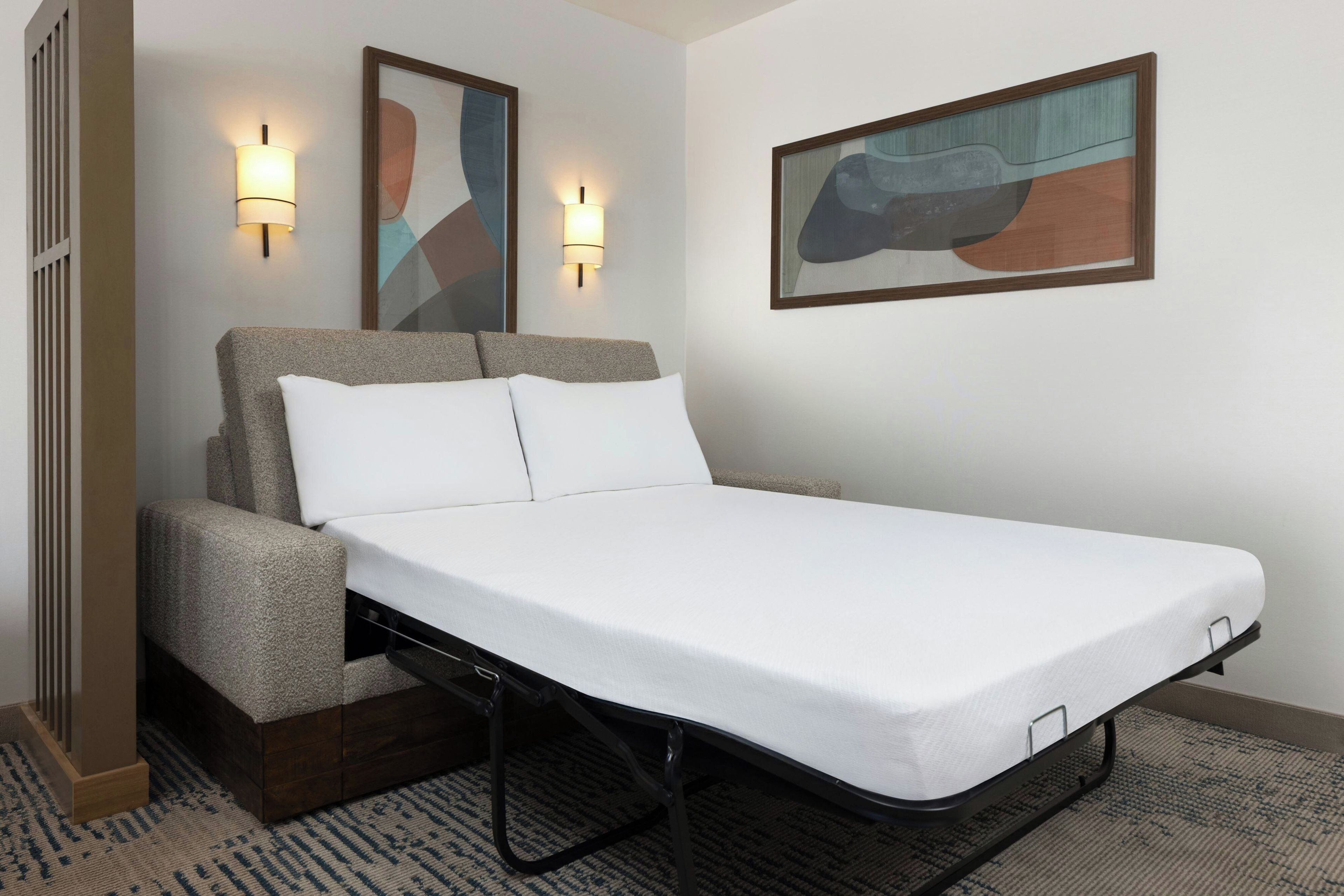 A single bed with a headboard, two wall-mounted lamps, and a framed abstract painting on the wall.