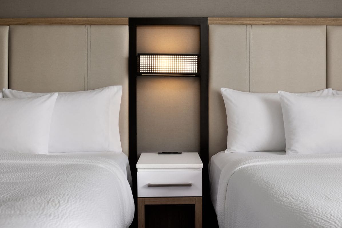 Een hotelkamer met twee bedden, een nachtkastje en een wandlamp.