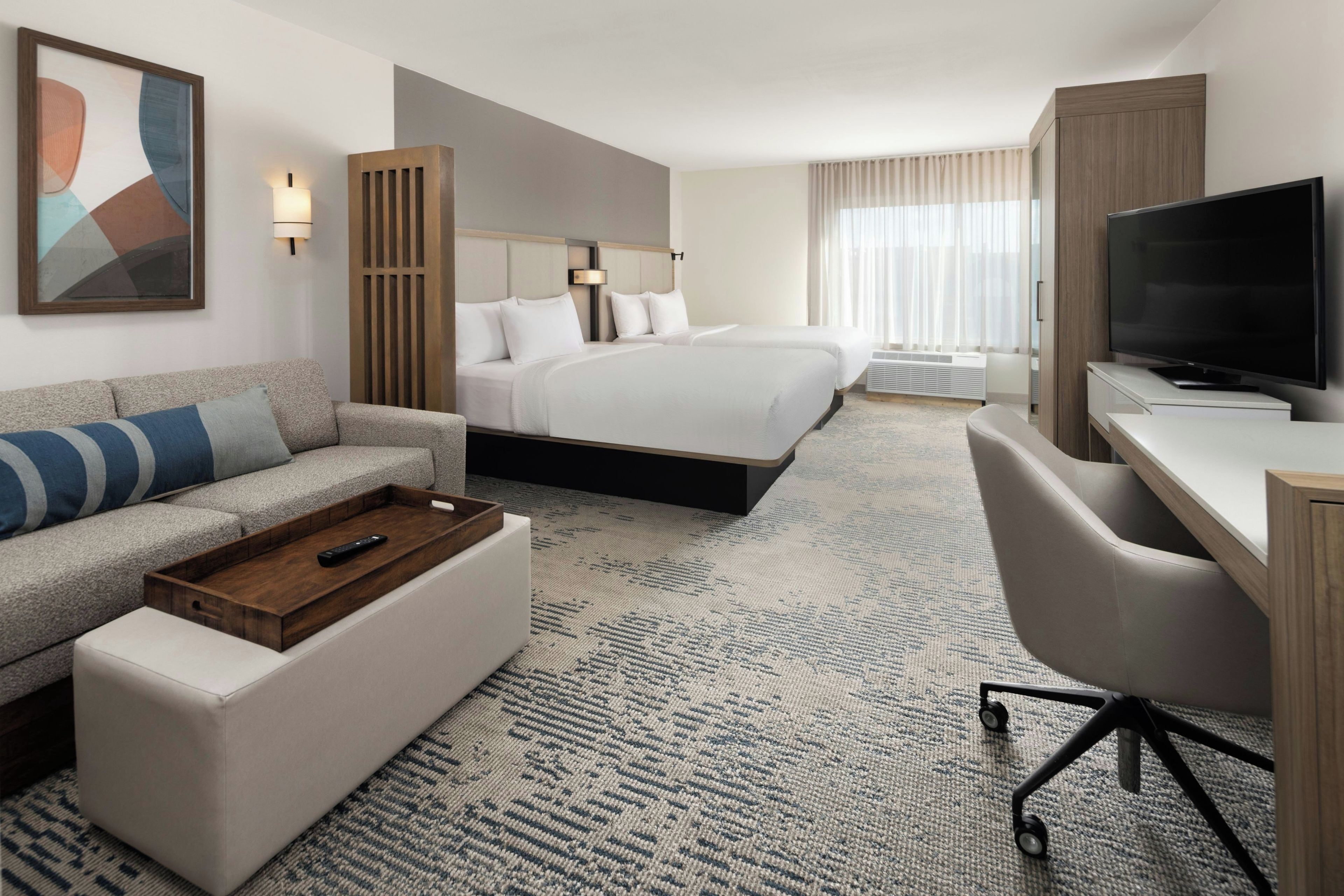 A hotel room with a bed, a sofa, a desk, a television, and a painting on the wall.