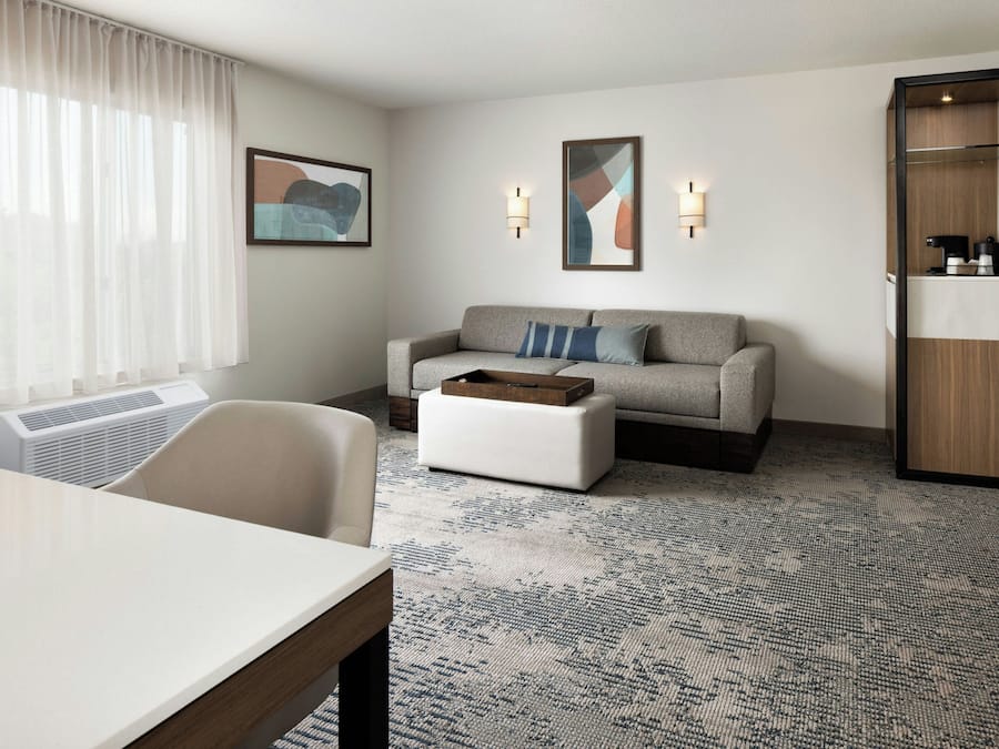 Ein Hotelzimmer mit einer Couch, einem Couchtisch, einem Esstisch und einem Schrank mit Pflegeprodukten.