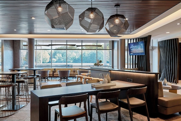 A modern restaurant with a large dining area, multiple tables and chairs, and a television screen on the wall.